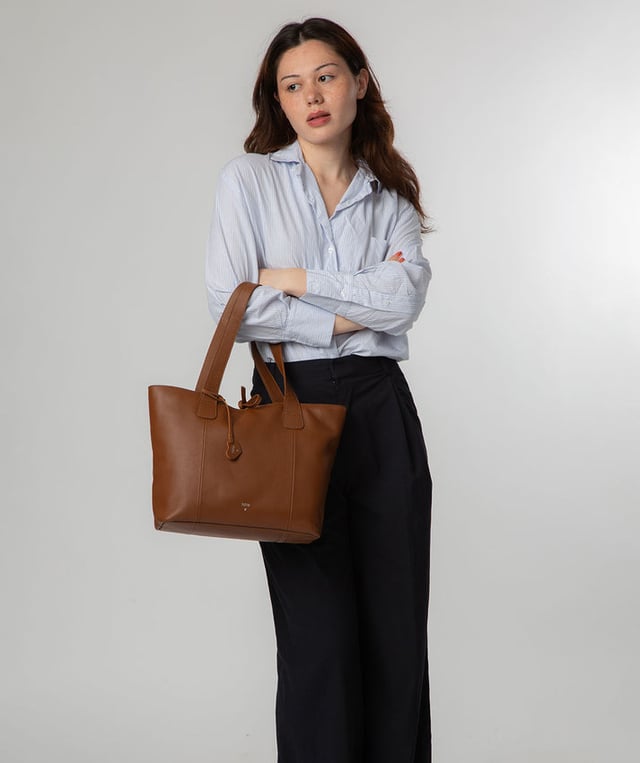 Handcrafted from natural leather with a soft to the touch pebble grain finish, the 'Carolina' tote bag from NiNa Amora is a must-have accessory. A unique tie top secures the central lined compartment which includes a zipped compartment which divides the design; perfect for maintaining an organised bag. Additional storage space is provided by a slip and zipped pocket on the interior, ideal for your phone, keys and any other essentials while out and about. Adorned with dual leather handles with a drop length of 25cm for a comfortable and versatile carrying options. Silver metal fittings and zips give this design a elegant look which is complemented the NiNa Amora X logo is silver foil embossed on the front and hanging charm for a luxurious finishing touch.