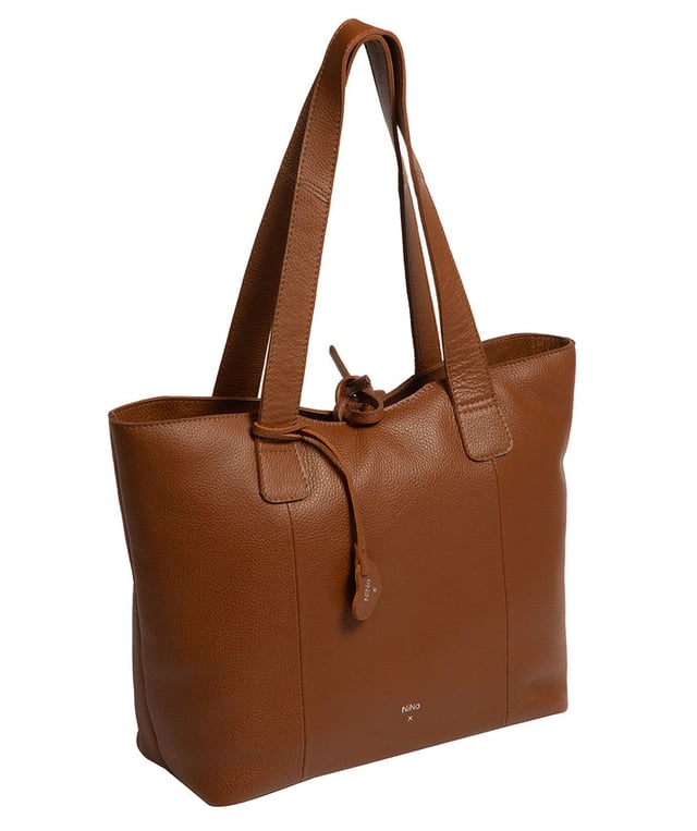 Handcrafted from natural leather with a soft to the touch pebble grain finish, the 'Carolina' tote bag from NiNa Amora is a must-have accessory. A unique tie top secures the central lined compartment which includes a zipped compartment which divides the design; perfect for maintaining an organised bag. Additional storage space is provided by a slip and zipped pocket on the interior, ideal for your phone, keys and any other essentials while out and about. Adorned with dual leather handles with a drop length of 25cm for a comfortable and versatile carrying options. Silver metal fittings and zips give this design a elegant look which is complemented the NiNa Amora X logo is silver foil embossed on the front and hanging charm for a luxurious finishing touch.