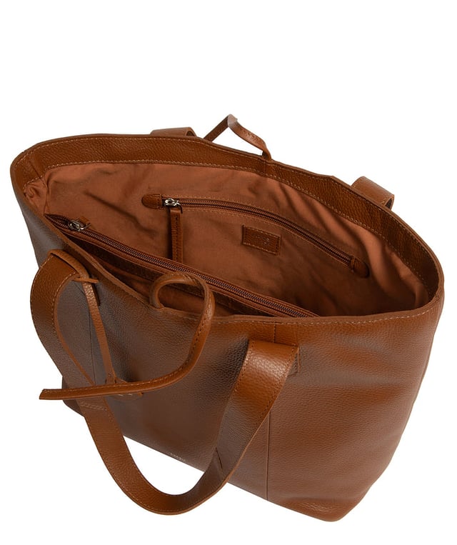 Handcrafted from natural leather with a soft to the touch pebble grain finish, the 'Carolina' tote bag from NiNa Amora is a must-have accessory. A unique tie top secures the central lined compartment which includes a zipped compartment which divides the design; perfect for maintaining an organised bag. Additional storage space is provided by a slip and zipped pocket on the interior, ideal for your phone, keys and any other essentials while out and about. Adorned with dual leather handles with a drop length of 25cm for a comfortable and versatile carrying options. Silver metal fittings and zips give this design a elegant look which is complemented the NiNa Amora X logo is silver foil embossed on the front and hanging charm for a luxurious finishing touch.