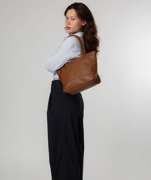 As part of the NiNa Amora brand, the 'Margarida' tote bag is inspired by our designer's daughter and all about elevating classic designs with high quality leather. A concealed zip-over top secures the spacious main lined compartment which opens to reveal additional storage space in the form of a slip and zipped pocket; ideal for your phone, keys and any other essentials. The classic angular sides of the tote are updated with this sophisticated design and adorned with slim leather handles with a drop length of 20cm. This bag is finished with sophisticated silver metal fittings and zips which are complemented by the NiNa Amora X logo embossed in silver on the front and on the hanging charm. Effortlessly chic.