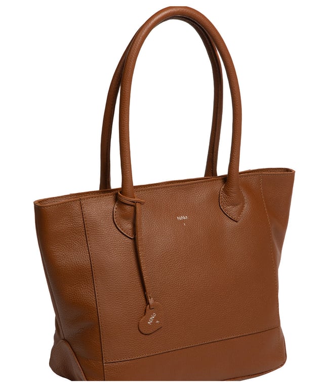 As part of the NiNa Amora brand, the 'Margarida' tote bag is inspired by our designer's daughter and all about elevating classic designs with high quality leather. A concealed zip-over top secures the spacious main lined compartment which opens to reveal additional storage space in the form of a slip and zipped pocket; ideal for your phone, keys and any other essentials. The classic angular sides of the tote are updated with this sophisticated design and adorned with slim leather handles with a drop length of 20cm. This bag is finished with sophisticated silver metal fittings and zips which are complemented by the NiNa Amora X logo embossed in silver on the front and on the hanging charm. Effortlessly chic.