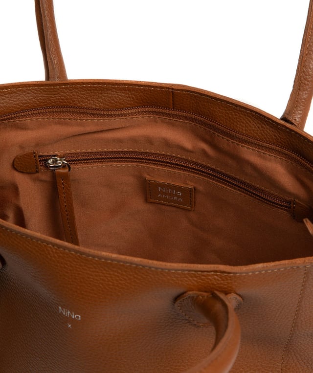 As part of the NiNa Amora brand, the 'Margarida' tote bag is inspired by our designer's daughter and all about elevating classic designs with high quality leather. A concealed zip-over top secures the spacious main lined compartment which opens to reveal additional storage space in the form of a slip and zipped pocket; ideal for your phone, keys and any other essentials. The classic angular sides of the tote are updated with this sophisticated design and adorned with slim leather handles with a drop length of 20cm. This bag is finished with sophisticated silver metal fittings and zips which are complemented by the NiNa Amora X logo embossed in silver on the front and on the hanging charm. Effortlessly chic.