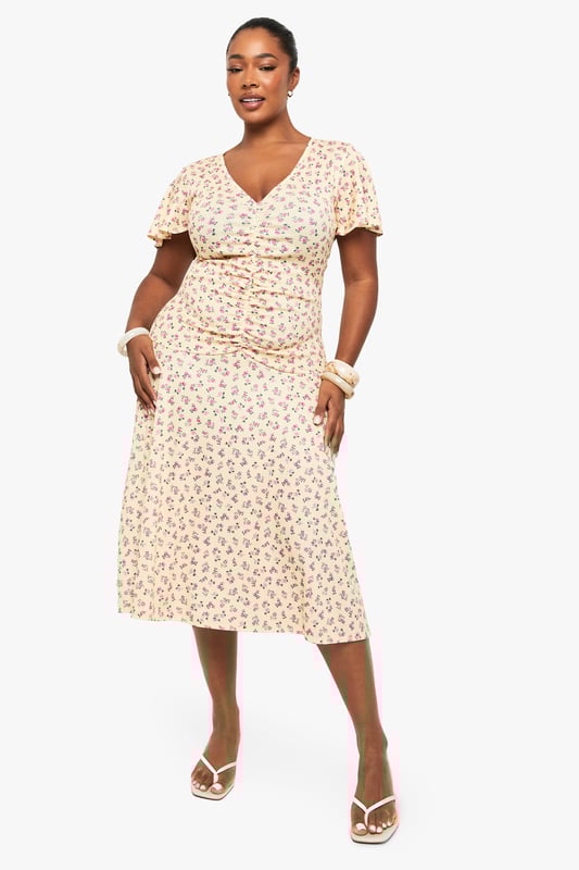 Flattering ruched detailing across the bodice for a figure-enhancing silhouette
        Feminine flutter sleeves adding movement and softness to the overall look
        Elegant V-neckline that frames the dcolletage beautifully
        Flowing midi-length skirt with gentle flare for ease of movement
        Versatile mesh fabric that drapes gracefully over curves
    
    This charming plus-size midi dress from Boohoo combines comfort with effortless style. The thoughtfully placed ruching creates a flattering shape while the delicate flutter sleeves add a touch of romance. Perfect for day-to-night versatility, pair with strappy sandals and a clutch as shown for daytime gatherings, or transform your look with statement jewellery and heeled boots for evening occasions. The flowing midi length offers both sophistication and practicality, making it ideal for office wear with a tailored blazer or weekend brunches with a denim jacket. The all-over pattern adds visual interest without overwhelming, whilst the V-neckline creates a balanced silhouette. This dress embodies Boohoo's commitment to inclusive fashion that transitions seamlessly between casual and more formal settings.