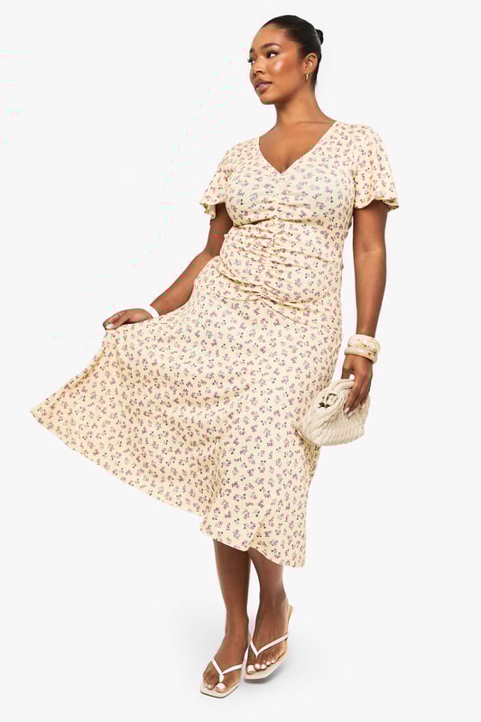 Flattering ruched detailing across the bodice for a figure-enhancing silhouette
        Feminine flutter sleeves adding movement and softness to the overall look
        Elegant V-neckline that frames the dcolletage beautifully
        Flowing midi-length skirt with gentle flare for ease of movement
        Versatile mesh fabric that drapes gracefully over curves
    
    This charming plus-size midi dress from Boohoo combines comfort with effortless style. The thoughtfully placed ruching creates a flattering shape while the delicate flutter sleeves add a touch of romance. Perfect for day-to-night versatility, pair with strappy sandals and a clutch as shown for daytime gatherings, or transform your look with statement jewellery and heeled boots for evening occasions. The flowing midi length offers both sophistication and practicality, making it ideal for office wear with a tailored blazer or weekend brunches with a denim jacket. The all-over pattern adds visual interest without overwhelming, whilst the V-neckline creates a balanced silhouette. This dress embodies Boohoo's commitment to inclusive fashion that transitions seamlessly between casual and more formal settings.