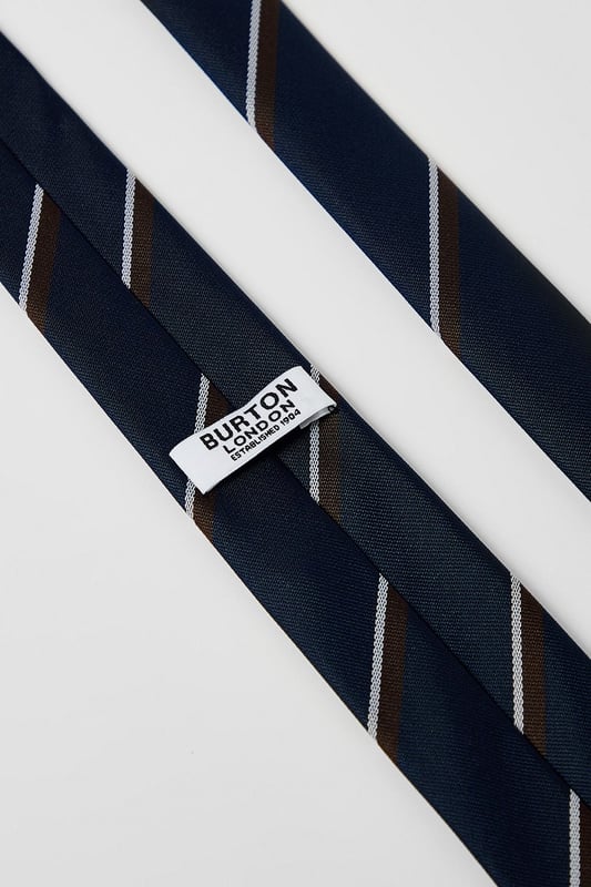 Classic navy tie featuring distinctive heritage diagonal stripes
        Standard width design suitable for both formal and smart-casual occasions
        Crafted with a smooth finish for easy knotting and a polished appearance
        Branded Burton label for authentic style credentials
        Machine washable at 30 degrees for convenient care
    
    This Burton Heritage Stripe Tie offers timeless British style with contemporary versatility. The diagonal stripe pattern presents a refined aesthetic that works brilliantly with a range of shirt options - pair with crisp white for important meetings or light blue for everyday office wear. The tie makes an excellent companion to a navy or grey suit for formal occasions, while also complementing more relaxed ensembles when worn with a blazer and chinos for family gatherings or weekend brunches. Perfect for the gentleman who appreciates classic styling with minimal fuss, this tie transitions seamlessly from daytime professional settings to casual evening drinks with colleagues. A wardrobe essential that reflects considered taste rather than fleeting trends - exactly what the modern British man requires from his accessories.