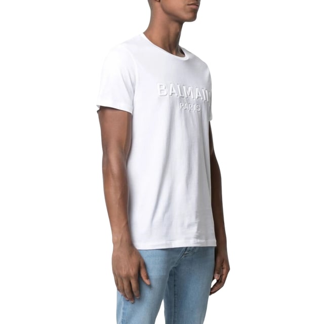 Balmain Paris Embossed Logo White T-shirt Elevate your wardrobe with the Balmain Paris Embossed Logo White T-Shirt, crafted from 100% premium cotton for exceptional comfort and breathability. Made in Portugal, this sleek white tee features a subtle yet striking embossed Balmain Paris logo, adding a touch of luxury to your everyday style. Its high-quality fabric ensures durability while maintaining a soft feel against the skin. Perfect for pairing with jeans or layering under jackets, this versatile t-shirt combines timeless design with modern sophistication, making it an essential piece for any fashion-conscious man. Experience effortless elegance with Balmain