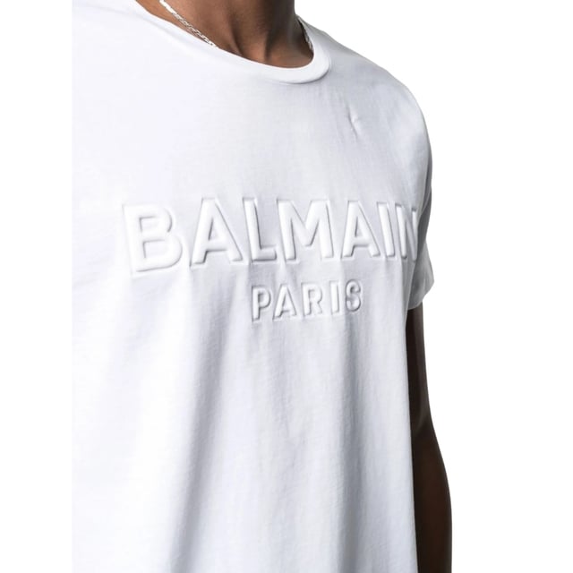 Balmain Paris Embossed Logo White T-shirt Elevate your wardrobe with the Balmain Paris Embossed Logo White T-Shirt, crafted from 100% premium cotton for exceptional comfort and breathability. Made in Portugal, this sleek white tee features a subtle yet striking embossed Balmain Paris logo, adding a touch of luxury to your everyday style. Its high-quality fabric ensures durability while maintaining a soft feel against the skin. Perfect for pairing with jeans or layering under jackets, this versatile t-shirt combines timeless design with modern sophistication, making it an essential piece for any fashion-conscious man. Experience effortless elegance with Balmain