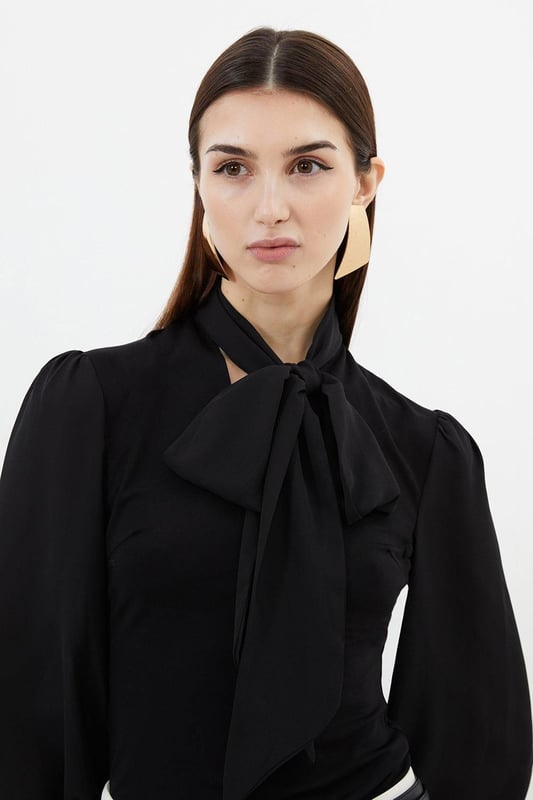 Jersey Ponte And Georgette Mix Tie Neck Long Sleeve Bodysuit This Karen Millen bodysuit combines classic elegance with contemporary styling. The contrasting textures of jersey and georgette create visual interest, while the statement pussy bow adds a touch of feminine charm. The balloon sleeves provide dramatic volume balanced by the fitted bodice, creating a flattering silhouette. Perfect for family gatherings or casual work events, this bodysuit can be dressed down with tailored denim and flats for weekend brunches, or paired with a pencil skirt for more refined occasions. The secure bodysuit design eliminates the need for constant re-tucking, ensuring you maintain a sleek appearance throughout the day. A versatile wardrobe staple that offers both comfort and sophistication. Jersey bodysuit featuring a georgette pussy bow detail Voluminous balloon sleeves with fitted cuffs and button detailing Round neckline Smooth, form-fitting designe