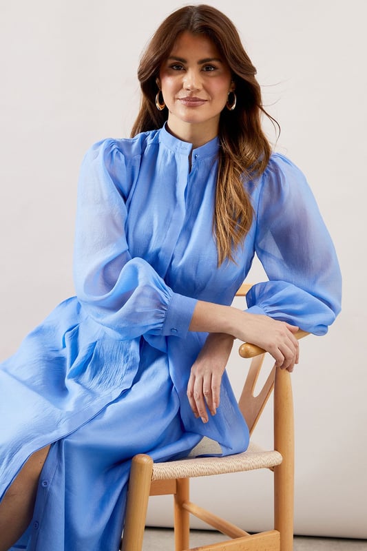 Elegant textured organza midi shirt dress with collarless neckline for a sophisticated silhouette
        Voluminous balloon sleeves with gathered cuffs create a dramatic yet refined look
        Flattering waist tie belt accentuates the figure while allowing for customised fit
        Practical side pockets discreetly integrated into the design
        Midi length offers versatility for both daytime and evening occasions
    
    This striking textured organza shirt dress combines contemporary elegance with timeless sophistication. The collarless design and button-through front create a clean, refined aesthetic, while the sumptuous balloon sleeves add a touch of drama to your ensemble. Cinch the included waist tie to create a beautifully defined silhouette that flatters all figures. Perfect for weddings and formal gatherings, style with delicate strappy heels as shown and statement earrings for a polished look. For race day events, complement with a fascinator and clutch bag. The versatile midi length works beautifully for graduation ceremonies or elegant garden parties. This Wallis piece transitions effortlessly from day to evening, making it a valuable addition to your occasion wardrobe that will serve you through multiple seasons with different accessories.