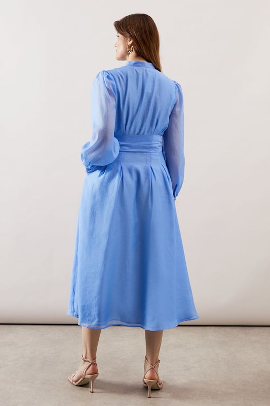 Elegant textured organza midi shirt dress with collarless neckline for a sophisticated silhouette
        Voluminous balloon sleeves with gathered cuffs create a dramatic yet refined look
        Flattering waist tie belt accentuates the figure while allowing for customised fit
        Practical side pockets discreetly integrated into the design
        Midi length offers versatility for both daytime and evening occasions
    
    This striking textured organza shirt dress combines contemporary elegance with timeless sophistication. The collarless design and button-through front create a clean, refined aesthetic, while the sumptuous balloon sleeves add a touch of drama to your ensemble. Cinch the included waist tie to create a beautifully defined silhouette that flatters all figures. Perfect for weddings and formal gatherings, style with delicate strappy heels as shown and statement earrings for a polished look. For race day events, complement with a fascinator and clutch bag. The versatile midi length works beautifully for graduation ceremonies or elegant garden parties. This Wallis piece transitions effortlessly from day to evening, making it a valuable addition to your occasion wardrobe that will serve you through multiple seasons with different accessories.