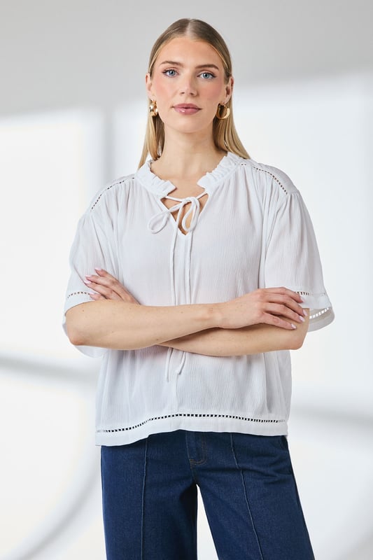 Distinctive ladder trim detailing along the neckline creates visual interest
        Relaxed regular fit with gathered shoulder design for effortless movement
        Elegant tie-front closure adds a feminine touch to this versatile blouse
        Short puff sleeves with trim detail offer a contemporary silhouette
        Textured woven fabric with gentle gathering at the back for added dimension
    
    This charming Principles blouse combines casual comfort with thoughtful design elements. The ladder trim detailing and tie-front feature create a relaxed yet put-together look that transitions seamlessly from day to evening. Style with white trousers and flat sandals as shown for a polished weekend ensemble, or pair with your favourite denim and trainers for casual coffee dates. The lightweight viscose fabric drapes beautifully, making it ideal for warmer days or layering under a cardigan when temperatures drop. Perfect for family gatherings, casual brunches or weekend shopping trips, this blouse offers the versatility to be dressed up with tailored trousers or kept casual with a denim skirt. The subtle textural elements and considered details reflect Principles' commitment to creating wardrobe staples with distinctive character.