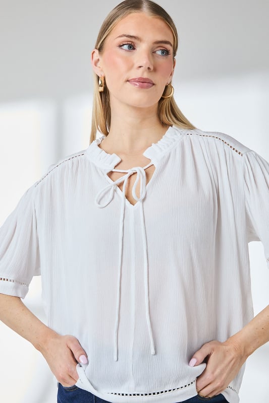 Distinctive ladder trim detailing along the neckline creates visual interest
        Relaxed regular fit with gathered shoulder design for effortless movement
        Elegant tie-front closure adds a feminine touch to this versatile blouse
        Short puff sleeves with trim detail offer a contemporary silhouette
        Textured woven fabric with gentle gathering at the back for added dimension
    
    This charming Principles blouse combines casual comfort with thoughtful design elements. The ladder trim detailing and tie-front feature create a relaxed yet put-together look that transitions seamlessly from day to evening. Style with white trousers and flat sandals as shown for a polished weekend ensemble, or pair with your favourite denim and trainers for casual coffee dates. The lightweight viscose fabric drapes beautifully, making it ideal for warmer days or layering under a cardigan when temperatures drop. Perfect for family gatherings, casual brunches or weekend shopping trips, this blouse offers the versatility to be dressed up with tailored trousers or kept casual with a denim skirt. The subtle textural elements and considered details reflect Principles' commitment to creating wardrobe staples with distinctive character.