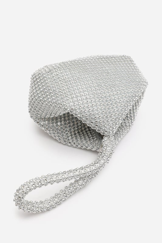 Add sparkle to your night with this Cascabel mini chainmail pouch bag, designed to dazzle at parties, weddings, or festive occasions. Its compact silhouette features shimmering crystal-style embellishments and a stylish knotted wristlet strap for easy carrying. Lightweight yet eye-catching, it's the perfect accessory for carrying your small essentials in glamorous style. A chic statement piece that blends retro charm with modern flair. Key Features: • Material: Rhinestone-embellished chainmail mesh • Dimensions: 16cm (L) x 14cm (H) x 10cm (W) • Fastening: Hidden zip closure at the top • Detail: Knotted wristlet strap for a secure and stylish hold