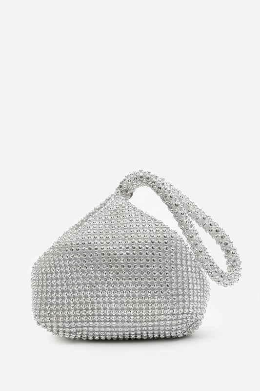 Add sparkle to your night with this Cascabel mini chainmail pouch bag, designed to dazzle at parties, weddings, or festive occasions. Its compact silhouette features shimmering crystal-style embellishments and a stylish knotted wristlet strap for easy carrying. Lightweight yet eye-catching, it's the perfect accessory for carrying your small essentials in glamorous style. A chic statement piece that blends retro charm with modern flair. Key Features: • Material: Rhinestone-embellished chainmail mesh • Dimensions: 16cm (L) x 14cm (H) x 10cm (W) • Fastening: Hidden zip closure at the top • Detail: Knotted wristlet strap for a secure and stylish hold