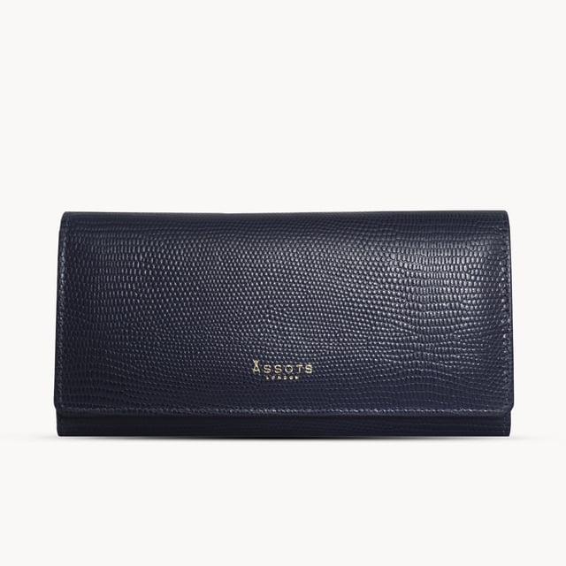 The ‘Claire’ flapover ladies purse is handcrafted with the premium lizard textured leather to give that designer look. Equipped with RFID technology, this practical ladies purse features a magnetic fastening closure with plenty of room to organise your cash, cards and coins. This large leather ladies purse is perfect to compliment your handbag and fits in easily. Stay safe and organised with ‘Claire’ the perfect addition to your collection of purses ideal for all outfits and occasions. Secured flap over magnetic fastening closure to store your essentials safely and securely. Foldover flap design. Equipped with RFID technology for safety. Additional back zip pocket to ensure you don’t run out of space. Two note compartments. Eight internal card compartments. Two windowed ID slots. Assots branded lined interiors. Lightweight for easy carry. Fittings Colour: Clean Brass. Composition: Body: 100% Genuine Leather. Lining: 100% Cotton. DISCLAIMER : All pictures shown are for illustration purpose only. Actual product colour may vary due to different ambience lighting or the screen display settings.