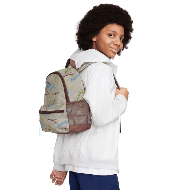 The Nike Youth All-Over Brand Logo Cream Bag combines style and practicality for young athletes and everyday use. Crafted from durable 100% polyester, this mini backpack features a cream base with a vibrant, multicoloured Nike Swoosh logo pattern that covers the entire bag, making it stand out. It offers a spacious 11-litre main compartment perfect for books, sports gear, or daily essentials, plus a secure front zip pocket for smaller items. Adjustable straps ensure a comfortable fit, while reliable zip fastenings keep belongings safe. Made in Vietnam, this backpack is a versatile and trendy choice for youth on the go