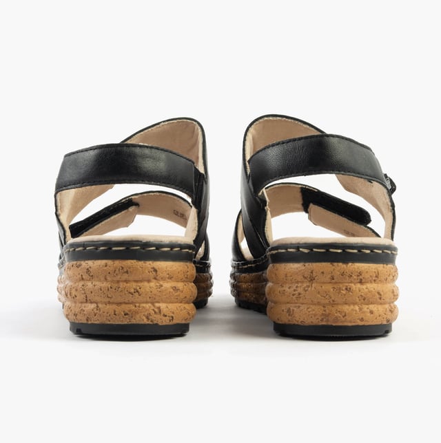 These open-toe women's sandals feature a leather upper, breathable lining, wedge heel, and extra-wide fit for comfort. Ideal for casual wear and easy to slip on with touch fasten closure