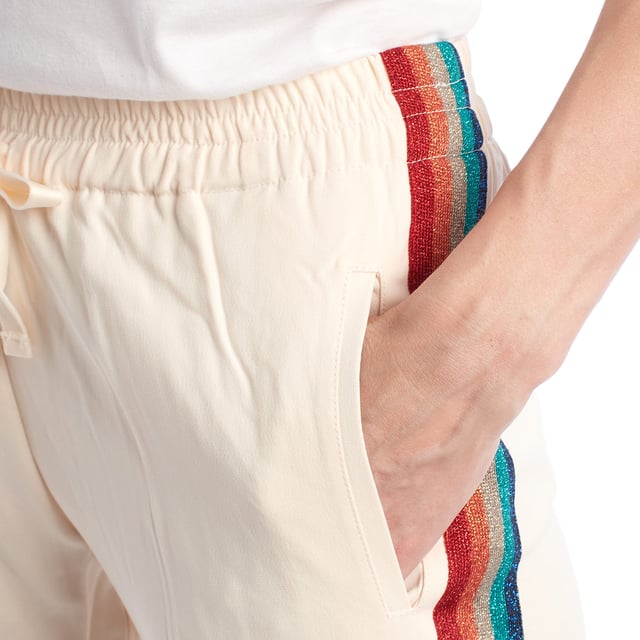 Pantalón fluido con banda lateral multicolor y cintura elástica.\n\nEste pantalón de estilo relajado combina comodidad y un diseño vibrante gracias a la banda lateral multicolor con acabado brillante. La cintura elástica con cordón ajustable proporciona un ajuste cómodo y favorecedor, ideal para looks casuales con un toque distintivo. Su corte recto estiliza la silueta sin renunciar al confort, y los bolsillos laterales aportan funcionalidad sin comprometer el diseño.\n\nDetalles:\n\nTipo de prenda: Pantalón largo fluido.\nMaterial: Tejido ligero con acabado satinado.\nEstilo: Deportivo chic.\nEstampado: Banda lateral con brillo multicolor.\nCintura: Elástica con cordón ajustable.\n\nUn pantalón mujer ideal para quienes buscan comodidad y estilo con un toque original. Perfecto para outfits urbanos con personalidad.\n Composición: 76% Acetato, 21% Viscosa, 3% Elastano\n Cuidados:\nLavar a mano en frío.\nNo usar lejía.\nNo secar en secadora.\nPlanchar a baja temperatura.