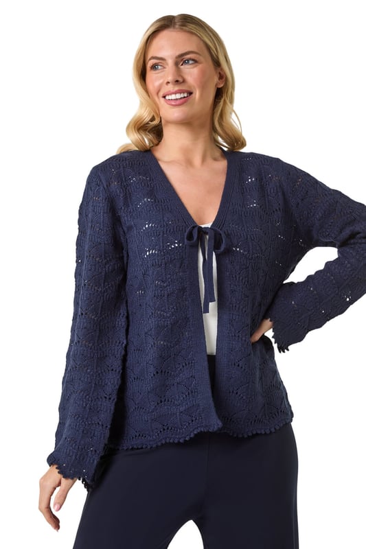 Petite Knitted Tie Cardigan from Roman. Elevate your knitwear collection with this charming v-neck cardigan. Crafted from a knitted fabric, this edge to edge cardigan features a unique tie fastening at the bust for added detail. The scallop style hem and pointelle detail along with the long sleeves make this cardigan a standout piece. Pair with jeans and sandals for a laid-back and stylish look this Spring/Summer season!