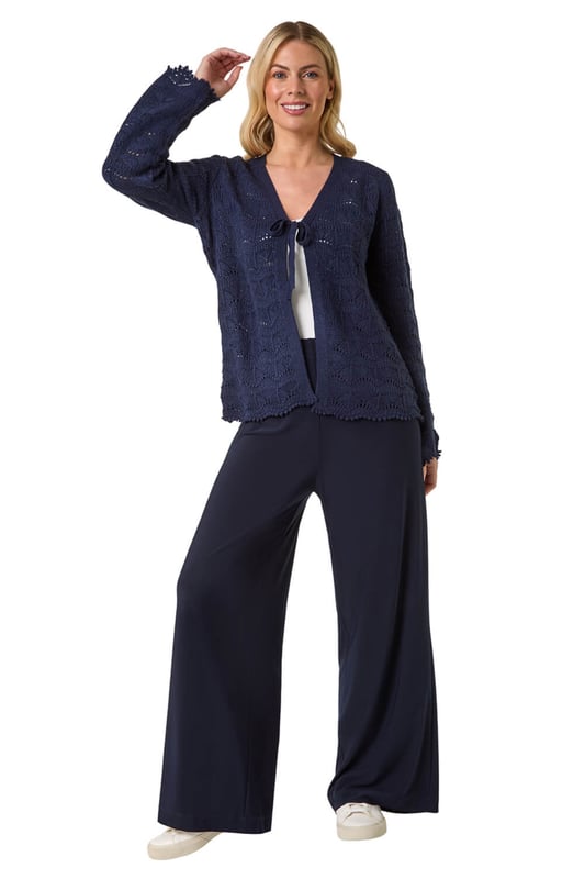 Petite Knitted Tie Cardigan from Roman. Elevate your knitwear collection with this charming v-neck cardigan. Crafted from a knitted fabric, this edge to edge cardigan features a unique tie fastening at the bust for added detail. The scallop style hem and pointelle detail along with the long sleeves make this cardigan a standout piece. Pair with jeans and sandals for a laid-back and stylish look this Spring/Summer season!