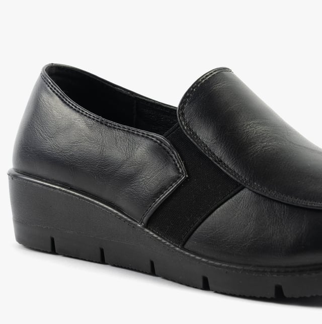 These casual women's slip-on shoes feature a leather upper, textile lining, rubber sole, and a low wedge heel, offering comfort and a wide fit for everyday wear