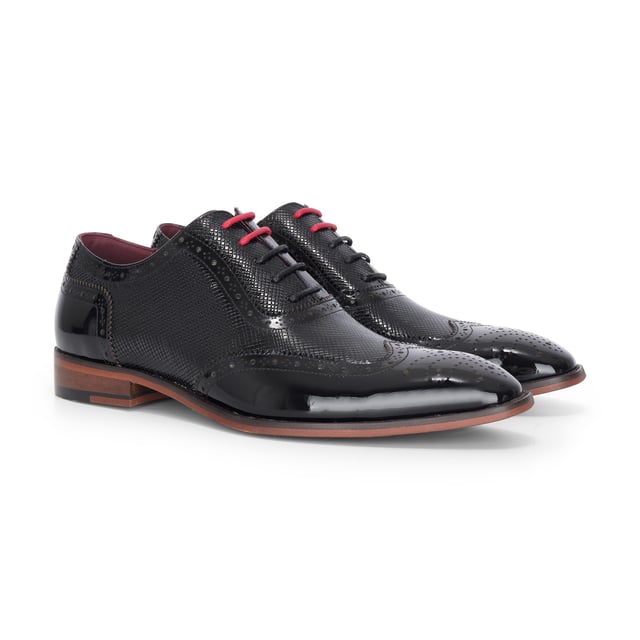 Realza tu look formal con los zapatos brogue Justin Reess Flynn de charol negro. Diseñados para una elegancia excepcional, estos zapatos presentan una parte superior de charol negro brillante con un sutil patrón texturizado, perfectos para bodas, eventos de gala o veladas sofisticadas. Los detalles brogue clásicos añaden un encanto tradicional, mientras que el diseño con cordones garantiza un ajuste seguro y a medida. Un suave forro interior aumenta la comodidad, haciéndolos ideales para un uso prolongado con confianza y estilo. Charol negro brillante con un sutil acabado texturizado para un look audaz y refinado. Brogue clásico. Perforaciones y costuras para una elegancia atemporal. Cierre seguro con cordones para un ajuste cómodo y ajustable. Interior con forro suave que aumenta la comodidad para usar todo el día. Silueta elegante perfecta para eventos formales, fiestas y ocasiones especiales. Confeccionados 100 % en cuero para mayor calidad y durabilidad.