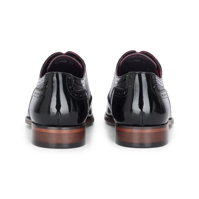 Realza tu look formal con los zapatos brogue Justin Reess Flynn de charol negro. Diseñados para una elegancia excepcional, estos zapatos presentan una parte superior de charol negro brillante con un sutil patrón texturizado, perfectos para bodas, eventos de gala o veladas sofisticadas. Los detalles brogue clásicos añaden un encanto tradicional, mientras que el diseño con cordones garantiza un ajuste seguro y a medida. Un suave forro interior aumenta la comodidad, haciéndolos ideales para un uso prolongado con confianza y estilo. Charol negro brillante con un sutil acabado texturizado para un look audaz y refinado. Brogue clásico. Perforaciones y costuras para una elegancia atemporal. Cierre seguro con cordones para un ajuste cómodo y ajustable. Interior con forro suave que aumenta la comodidad para usar todo el día. Silueta elegante perfecta para eventos formales, fiestas y ocasiones especiales. Confeccionados 100 % en cuero para mayor calidad y durabilidad.