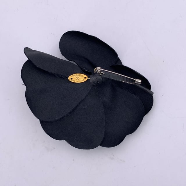 VINTAGE, RRP AS NEW
Elegant and unmistakably classic, this vintage Chanel Camellia brooch captures the essence of the house's refined femininity. The Camellia - a symbol of Chanel's enduring muse - blooms here in soft black silk, its petals gently layered to evoke quiet sophistication and grace.  With a generous diameter of 3.5 inches (8.9 cm), this statement piece is secured with a traditional safety pin closure. The reverse bears the iconic 'CHANEL - CC - Made in France' oval tab, marking its ity and Parisian heritage. A quintessential vintage treasure, perfect for adorning lapels, scarves, or bags with timeless allure. Condition Rating: A - EXCELLENTCondition Details: Gently used. Chanel box included. Please check the photos carefully and ask if you need to know more details or if you have any doubts.  Box?: ?: Yes