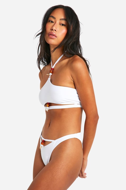 Hipster-style bikini bottoms with distinctive shell embellishments for a beach-ready aesthetic
        Low-rise fit that sits comfortably on the hips for a flattering silhouette
        Decorative shell details add a touch of coastal charm to your swimwear collection
        Coordinating top features a halter neck design with matching shell accents
        Moderate coverage at the back provides the perfect balance between style and comfort
    
    Make waves this holiday season with these eye-catching hipster bikini bottoms from Boohoo. The standout shell embellishments create a captivating coastal vibe that's perfect for beach days and poolside lounging. Pair with the matching halter top for a coordinated look that's both stylish and practical for swimming. The clean lines and contemporary design make this set versatile enough to mix with other swimwear pieces in your collection. For a complete beach day ensemble, throw on a lightweight kimono and strappy sandals when heading to the beach bar, or style with high-waisted linen trousers and oversized sunglasses for a sophisticated resort look. Whether you're planning a tropical getaway or simply soaking up the sun at a local lido, these bikini bottoms will ensure you look fabulous whilst making the most of your holiday.