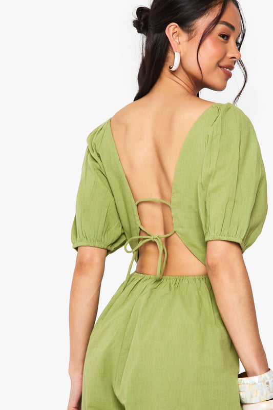 Crafted from a breathable linen mix fabric, perfect for warm-weather occasions
        Featuring charming puff sleeves for a feminine, on-trend silhouette
        Flattering V-neckline frames the dcolletage beautifully
        Striking open back design with delicate tie detail for added interest
        Relaxed fit shorts provide comfort whilst maintaining a stylish appearance
    
    This delightful linen mix playsuit combines comfort with effortless style for your casual wardrobe. The feminine puff sleeves create a romantic silhouette, while the plunging V-neckline adds a touch of allure. The standout feature is undoubtedly the open back with tie detailing, creating visual interest when you turn around. Style with flat sandals and a woven bag, as shown on our model, for daytime gatherings or family brunches. For a more polished look, add statement earrings and metallic accessories. The versatile design works brilliantly for garden parties, seaside holidays or casual weekend outings. The breathable fabric ensures you'll stay comfortable throughout the day, making this playsuit a summer wardrobe essential that delivers both practicality and style in equal measure.