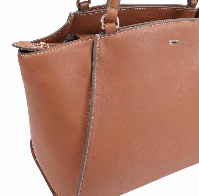 This uniquely shaped leather tote bag combines elegance with practicality, featuring a spacious central compartment secured by a top zip, perfect for work or casual outings. It offers convenient organization with external slip pockets on both sides, an internal zip pocket, and an additional slip pocket inside. Designed for comfort, the long shoulder handles make it easy to carry all day, while the clean silhouette is elevated by a sleek metal logo pin for a touch of refined style. D:18cm W:42.5cm H:27.5