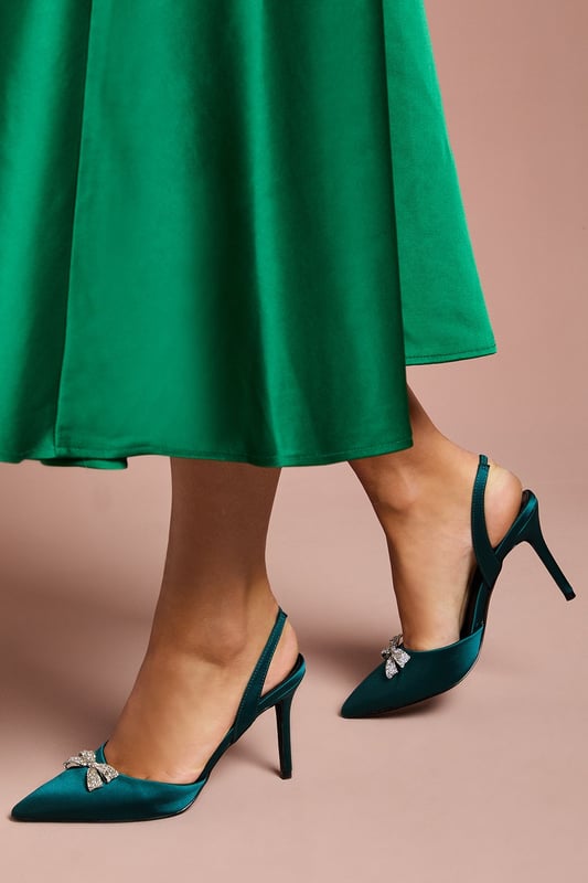 Elegant satin slingback court shoes featuring a stunning diamante bow brooch detail
        Pointed toe silhouette creates a flattering, elongated look
        Sophisticated 8cm stiletto heel adds height whilst maintaining comfort
        Wide fit design offers additional room for all-day wear
        Secure slingback strap with elasticated insert ensures the perfect fit
    
    The Scarlett slingback heels from Coast are the epitome of occasion-worthy footwear. These striking court shoes combine timeless elegance with contemporary flair, featuring a luxurious satin finish and eye-catching diamante bow brooch that catches the light beautifully with every step. The pointed toe and sleek stiletto heel create a refined silhouette that complements both midi and full-length gowns perfectly. Style with a tailored dress for a wedding or pair with a structured jumpsuit for the races. The wide fit construction ensures comfort throughout formal events, whilst the slingback design adds a touch of vintage charm. These versatile heels transition effortlessly from daytime ceremonies to evening receptions, making them a worthy investment for your special occasion wardrobe.