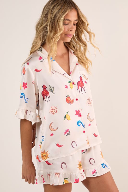 Luxurious satin finish with playful western-inspired conversational print featuring fruits, suns, and desert motifs
        Relaxed button-up short sleeve top with charming ruffle trim detailing
        Matching shorts with ruffle hem for a coordinated nightwear look
        Comfortable loose fit designed for ease of movement during sleep
        Collared neckline with classic front button closure for adjustable styling
    
    Drift into dreamland with this delightfully whimsical Satin Western Conversational Ruffle Pajama Shorts Set from Nasty Gal. The charming print showcases a playful array of western-inspired motifs, creating a fun yet sophisticated nightwear option. The relaxed silhouette features a button-up top with short sleeves and a classic collar, whilst the coordinating shorts offer the perfect balance of comfort and style. The ruffle detailing adds a feminine touch to this set, making bedtime feel that little bit more special. Perfect for warm summer evenings or cosy nights in, this set can be worn whilst lounging with a good book and a cup of tea, or for those lazy weekend mornings when breakfast in bed is calling. For chillier nights, simply pair with fluffy socks and a lightweight dressing gown for additional warmth without compromising on style.