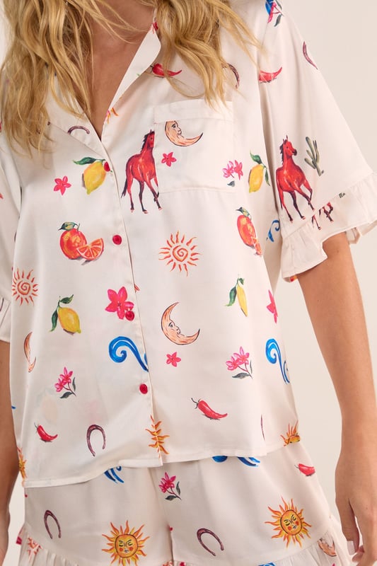 Luxurious satin finish with playful western-inspired conversational print featuring fruits, suns, and desert motifs
        Relaxed button-up short sleeve top with charming ruffle trim detailing
        Matching shorts with ruffle hem for a coordinated nightwear look
        Comfortable loose fit designed for ease of movement during sleep
        Collared neckline with classic front button closure for adjustable styling
    
    Drift into dreamland with this delightfully whimsical Satin Western Conversational Ruffle Pajama Shorts Set from Nasty Gal. The charming print showcases a playful array of western-inspired motifs, creating a fun yet sophisticated nightwear option. The relaxed silhouette features a button-up top with short sleeves and a classic collar, whilst the coordinating shorts offer the perfect balance of comfort and style. The ruffle detailing adds a feminine touch to this set, making bedtime feel that little bit more special. Perfect for warm summer evenings or cosy nights in, this set can be worn whilst lounging with a good book and a cup of tea, or for those lazy weekend mornings when breakfast in bed is calling. For chillier nights, simply pair with fluffy socks and a lightweight dressing gown for additional warmth without compromising on style.