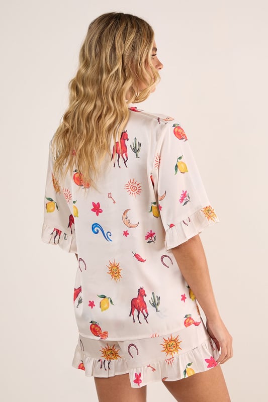 Luxurious satin finish with playful western-inspired conversational print featuring fruits, suns, and desert motifs
        Relaxed button-up short sleeve top with charming ruffle trim detailing
        Matching shorts with ruffle hem for a coordinated nightwear look
        Comfortable loose fit designed for ease of movement during sleep
        Collared neckline with classic front button closure for adjustable styling
    
    Drift into dreamland with this delightfully whimsical Satin Western Conversational Ruffle Pajama Shorts Set from Nasty Gal. The charming print showcases a playful array of western-inspired motifs, creating a fun yet sophisticated nightwear option. The relaxed silhouette features a button-up top with short sleeves and a classic collar, whilst the coordinating shorts offer the perfect balance of comfort and style. The ruffle detailing adds a feminine touch to this set, making bedtime feel that little bit more special. Perfect for warm summer evenings or cosy nights in, this set can be worn whilst lounging with a good book and a cup of tea, or for those lazy weekend mornings when breakfast in bed is calling. For chillier nights, simply pair with fluffy socks and a lightweight dressing gown for additional warmth without compromising on style.
