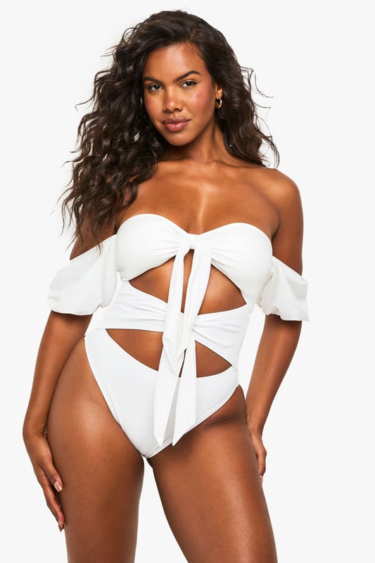 Elegant tanga swimsuit designed specifically for bridal occasions
        Striking off-shoulder design with delicate puff sleeves for a romantic touch
        Distinctive front bow detail creating a sophisticated cut-out effect
        High-cut leg design for an elongating silhouette
        Flattering high-waisted back for comfortable coverage
    
    Make a statement on your special day with this show-stopping bridal tanga swimsuit from Boohoo. Perfect for honeymoon beach days or pre-wedding poolside celebrations, this distinctive piece combines contemporary design with bridal elegance. The charming off-shoulder style with soft puff sleeves creates a feminine silhouette, whilst the decorative bow detailing and strategic cut-outs add a modern twist to traditional bridal swimwear. The high-cut leg design elongates your figure beautifully, whilst the high-waisted back ensures you feel confident and comfortable throughout your celebration. Pair with oversized sunglasses and a flowing kimono for poolside glamour, or style with a sheer sarong and delicate anklet for beachside sophistication. This swimsuit transitions effortlessly from daytime sunbathing to sunset cocktails, ensuring you look and feel fabulous throughout your bridal celebrations.