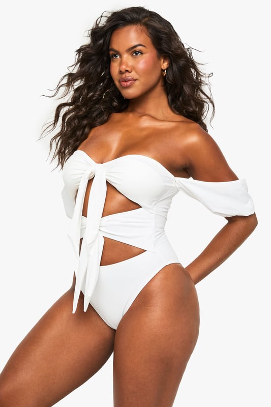 Elegant tanga swimsuit designed specifically for bridal occasions
        Striking off-shoulder design with delicate puff sleeves for a romantic touch
        Distinctive front bow detail creating a sophisticated cut-out effect
        High-cut leg design for an elongating silhouette
        Flattering high-waisted back for comfortable coverage
    
    Make a statement on your special day with this show-stopping bridal tanga swimsuit from Boohoo. Perfect for honeymoon beach days or pre-wedding poolside celebrations, this distinctive piece combines contemporary design with bridal elegance. The charming off-shoulder style with soft puff sleeves creates a feminine silhouette, whilst the decorative bow detailing and strategic cut-outs add a modern twist to traditional bridal swimwear. The high-cut leg design elongates your figure beautifully, whilst the high-waisted back ensures you feel confident and comfortable throughout your celebration. Pair with oversized sunglasses and a flowing kimono for poolside glamour, or style with a sheer sarong and delicate anklet for beachside sophistication. This swimsuit transitions effortlessly from daytime sunbathing to sunset cocktails, ensuring you look and feel fabulous throughout your bridal celebrations.