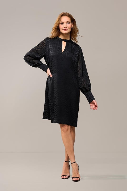 Wählen Sie diese Saison das Abilene-Kleid in klassischem Schwarz. Dieses stilvolle Kleid vereint mühelos Eleganz und Komfort mit einem wunderschönen glänzenden Polka-Dot-Motiv auf einem halbtransparenten Stoff. Das Design verfügt über einen Stehkragen und dezente Schlüssellochöffnungen vorne und hinten, die für einen raffinierten und einzigartigen Look sorgen. Die langen Ballonärmel und breiten Bündchen sorgen für einen modischen Touch, während die knielange und lockere Passform ein angenehmes Tragegefühl garantiert. Das glänzende Polka-Dot-Motiv verleiht dem Kleid einen luxuriösen Designer-Look und macht es zu einem echten Hingucker. Kombinieren Sie das Kleid tagsüber mit robusten Stiefeln und einer Jeansjacke für ein lässig-schickes Outfit oder tragen Sie es abends mit eleganten Heels für ein sommerliches Dinner-Date oder einen schönen Abenddrink. Mit einem Gürtel können Sie eine schmeichelnde Sanduhrfigur kreieren, das Kleid kann aber auch bequem locker getragen werden. Fashion-Tipp: Entdecken Sie auch die grüne Variante dieses Kleides oder entscheiden Sie sich für die stylische schwarze Bluse mit dem gleichen verspielten Polka-Dot-Motiv!