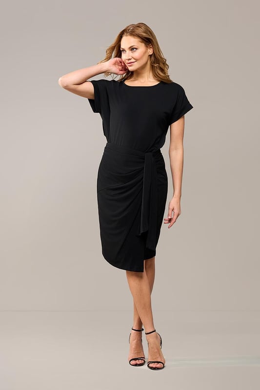 De elegante zwarte Riley rok is zowel casual als sportief en is een must-have in je garderobe. Deze rok heeft een mooie lengte die net boven de knie valt en is gemaakt van een hoogwaardige jersey stof die ultiem comfort biedt. De fijne stretch in de stof zorgt ervoor dat de rok soepel om je lichaam valt, waardoor je hem niet wilt uittrekken. Het asymmetrische strikdetail aan de linkerzijde van de overslagrok geeft een uniek en stijlvol effect. De rok heeft een rechte pasvorm en is voorzien van een elastisch detail in de tailleband aan de achterkant voor optimaal draagcomfort. Het rechte model staat garant voor een perfecte pasvorm en maximale draagbaarheid. Combineer de stijlvolle Riley overslagrok met de zwarte Raisy top voor een speelse jurk-look, of draag hem met een blazer en laarsjes voor een chique, afgewerkte look. Je kunt de zwarte rok ook combineren met een mooie blouse en een laars voor een elegante kantooroutfit. Ga voor een look die zowel comfortabel als chic is!