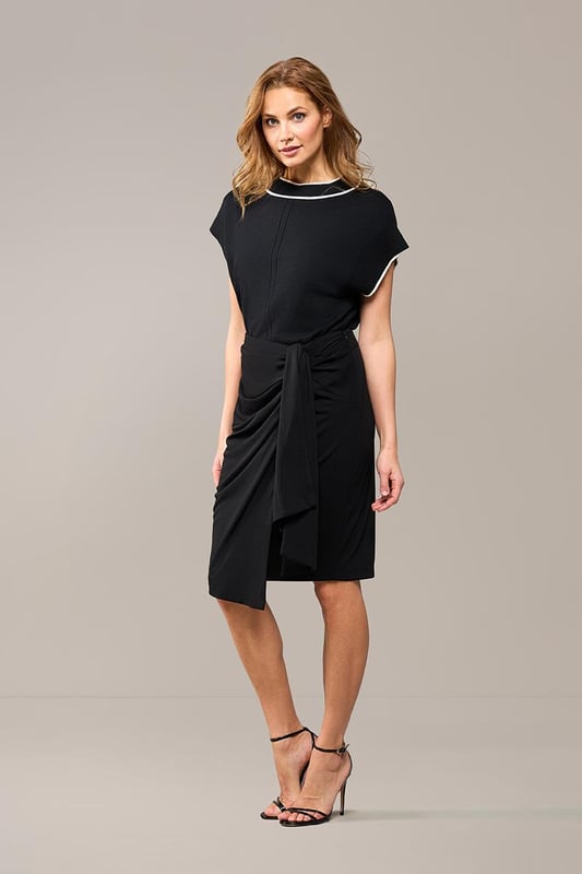 De elegante zwarte Riley rok is zowel casual als sportief en is een must-have in je garderobe. Deze rok heeft een mooie lengte die net boven de knie valt en is gemaakt van een hoogwaardige jersey stof die ultiem comfort biedt. De fijne stretch in de stof zorgt ervoor dat de rok soepel om je lichaam valt, waardoor je hem niet wilt uittrekken. Het asymmetrische strikdetail aan de linkerzijde van de overslagrok geeft een uniek en stijlvol effect. De rok heeft een rechte pasvorm en is voorzien van een elastisch detail in de tailleband aan de achterkant voor optimaal draagcomfort. Het rechte model staat garant voor een perfecte pasvorm en maximale draagbaarheid. Combineer de stijlvolle Riley overslagrok met de zwarte Raisy top voor een speelse jurk-look, of draag hem met een blazer en laarsjes voor een chique, afgewerkte look. Je kunt de zwarte rok ook combineren met een mooie blouse en een laars voor een elegante kantooroutfit. Ga voor een look die zowel comfortabel als chic is!