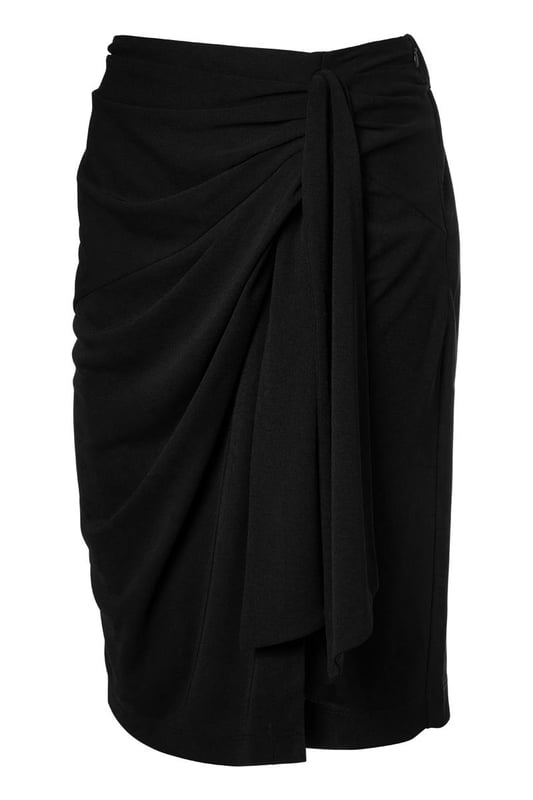 De elegante zwarte Riley rok is zowel casual als sportief en is een must-have in je garderobe. Deze rok heeft een mooie lengte die net boven de knie valt en is gemaakt van een hoogwaardige jersey stof die ultiem comfort biedt. De fijne stretch in de stof zorgt ervoor dat de rok soepel om je lichaam valt, waardoor je hem niet wilt uittrekken. Het asymmetrische strikdetail aan de linkerzijde van de overslagrok geeft een uniek en stijlvol effect. De rok heeft een rechte pasvorm en is voorzien van een elastisch detail in de tailleband aan de achterkant voor optimaal draagcomfort. Het rechte model staat garant voor een perfecte pasvorm en maximale draagbaarheid. Combineer de stijlvolle Riley overslagrok met de zwarte Raisy top voor een speelse jurk-look, of draag hem met een blazer en laarsjes voor een chique, afgewerkte look. Je kunt de zwarte rok ook combineren met een mooie blouse en een laars voor een elegante kantooroutfit. Ga voor een look die zowel comfortabel als chic is!