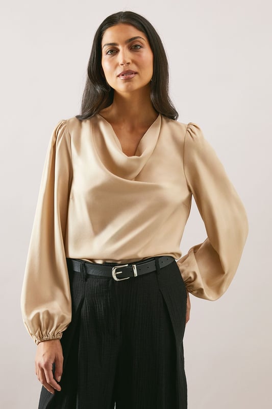 Elegant cowl neckline that drapes beautifully for a sophisticated silhouette
        Statement balloon sleeves with delicate gathered cuffs for a touch of drama
        Lustrous satin finish that catches the light with subtle sheen
        Versatile loose fit that flatters all body types
        Clean-lined design with a smooth back for effortless styling
    
    This Wallis satin blouse combines timeless elegance with contemporary styling. The graceful cowl neckline creates a flattering drape that frames your dcolletage beautifully, whilst the voluminous balloon sleeves add a touch of refined drama to your ensemble. Style as seen with wide-leg trousers and a slim belt for a balanced silhouette that works wonderfully for family gatherings or lunch with friends. The fluid fabric moves gracefully with you, making this piece ideal for daytime events where comfort and style are equally important. Pair with tailored trousers and flats for work, or dress down with your favourite denim and trainers for weekend brunches. This versatile blouse transitions effortlessly from day to evening, making it a wardrobe essential for the modern woman who values both sophistication and comfort.