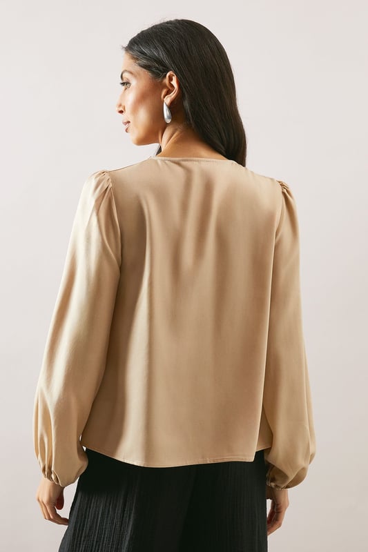 Elegant cowl neckline that drapes beautifully for a sophisticated silhouette
        Statement balloon sleeves with delicate gathered cuffs for a touch of drama
        Lustrous satin finish that catches the light with subtle sheen
        Versatile loose fit that flatters all body types
        Clean-lined design with a smooth back for effortless styling
    
    This Wallis satin blouse combines timeless elegance with contemporary styling. The graceful cowl neckline creates a flattering drape that frames your dcolletage beautifully, whilst the voluminous balloon sleeves add a touch of refined drama to your ensemble. Style as seen with wide-leg trousers and a slim belt for a balanced silhouette that works wonderfully for family gatherings or lunch with friends. The fluid fabric moves gracefully with you, making this piece ideal for daytime events where comfort and style are equally important. Pair with tailored trousers and flats for work, or dress down with your favourite denim and trainers for weekend brunches. This versatile blouse transitions effortlessly from day to evening, making it a wardrobe essential for the modern woman who values both sophistication and comfort.