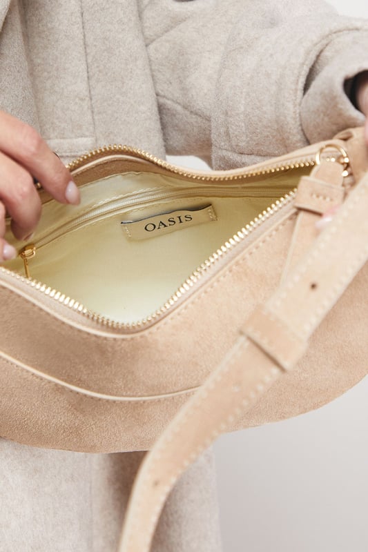 Distinctive half-moon silhouette for a contemporary aesthetic
        Soft faux suede texture adds a luxurious touch to casual outfits
        Adjustable crossbody strap for comfortable all-day wear
        Secure zip-top closure to keep essentials safe
        Compact yet spacious enough for daily necessities
    
    The Relly Faux Suede Half Moon Crossbody Bag combines practicality with feminine charm, embodying Oasis's signature style. The curved silhouette creates a soft, modern look that pairs beautifully with both casual and smart-casual ensembles. Style with relaxed denim and a floaty blouse for daytime outings, or match with a floral day dress for garden parties and family gatherings. The versatile design makes it perfect for weekend shopping trips, coffee dates, or casual lunches. The adjustable strap allows for customised wear, while the interior provides just enough room for your phone, wallet, keys and lipstick. This bag effortlessly transitions from day to evening, making it an essential addition to your accessory collection for those moments when you want to travel light without compromising on style.
