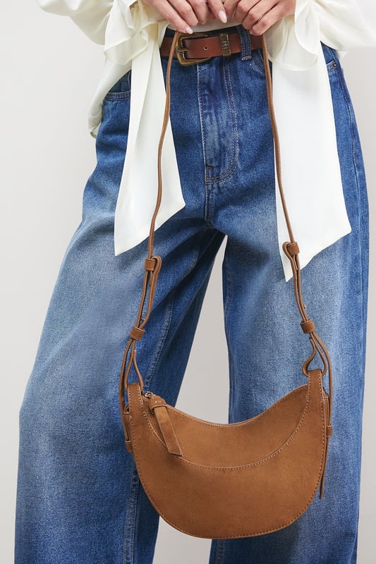 Distinctive half-moon silhouette for a contemporary aesthetic
        Soft faux suede texture adds a luxurious touch to casual outfits
        Adjustable crossbody strap for comfortable all-day wear
        Secure zip-top closure to keep essentials safe
        Compact yet spacious enough for daily necessities
    
    The Relly Faux Suede Half Moon Crossbody Bag combines practicality with feminine charm, embodying Oasis's signature style. The curved silhouette creates a soft, modern look that pairs beautifully with both casual and smart-casual ensembles. Style with relaxed denim and a floaty blouse for daytime outings, or match with a floral day dress for garden parties and family gatherings. The versatile design makes it perfect for weekend shopping trips, coffee dates, or casual lunches. The adjustable strap allows for customised wear, while the interior provides just enough room for your phone, wallet, keys and lipstick. This bag effortlessly transitions from day to evening, making it an essential addition to your accessory collection for those moments when you want to travel light without compromising on style.