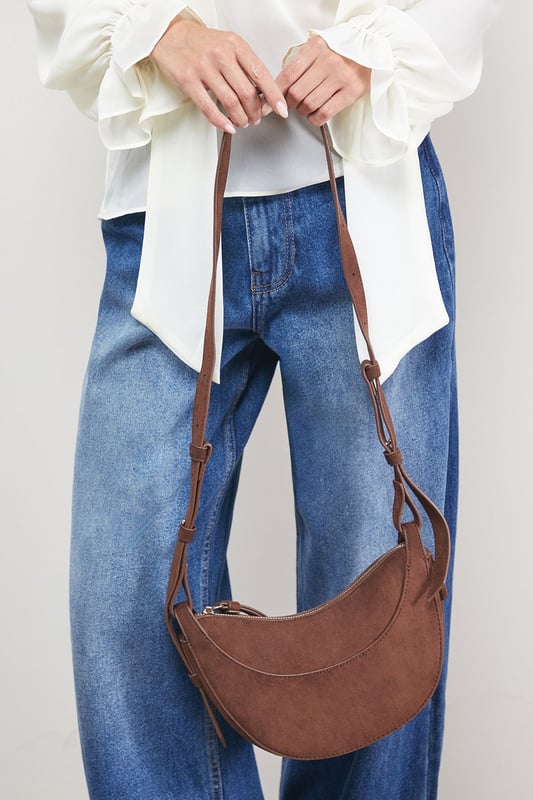 Distinctive half-moon silhouette for a contemporary aesthetic
        Soft faux suede texture adds a luxurious touch to casual outfits
        Adjustable crossbody strap for comfortable all-day wear
        Secure zip-top closure to keep essentials safe
        Compact yet spacious enough for daily necessities
    
    The Relly Faux Suede Half Moon Crossbody Bag combines practicality with feminine charm, embodying Oasis's signature style. The curved silhouette creates a soft, modern look that pairs beautifully with both casual and smart-casual ensembles. Style with relaxed denim and a floaty blouse for daytime outings, or match with a floral day dress for garden parties and family gatherings. The versatile design makes it perfect for weekend shopping trips, coffee dates, or casual lunches. The adjustable strap allows for customised wear, while the interior provides just enough room for your phone, wallet, keys and lipstick. This bag effortlessly transitions from day to evening, making it an essential addition to your accessory collection for those moments when you want to travel light without compromising on style.