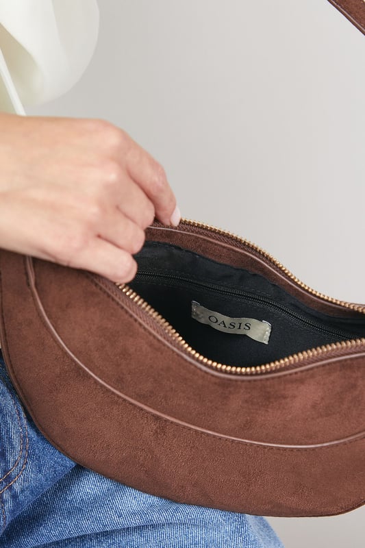 Distinctive half-moon silhouette for a contemporary aesthetic
        Soft faux suede texture adds a luxurious touch to casual outfits
        Adjustable crossbody strap for comfortable all-day wear
        Secure zip-top closure to keep essentials safe
        Compact yet spacious enough for daily necessities
    
    The Relly Faux Suede Half Moon Crossbody Bag combines practicality with feminine charm, embodying Oasis's signature style. The curved silhouette creates a soft, modern look that pairs beautifully with both casual and smart-casual ensembles. Style with relaxed denim and a floaty blouse for daytime outings, or match with a floral day dress for garden parties and family gatherings. The versatile design makes it perfect for weekend shopping trips, coffee dates, or casual lunches. The adjustable strap allows for customised wear, while the interior provides just enough room for your phone, wallet, keys and lipstick. This bag effortlessly transitions from day to evening, making it an essential addition to your accessory collection for those moments when you want to travel light without compromising on style.