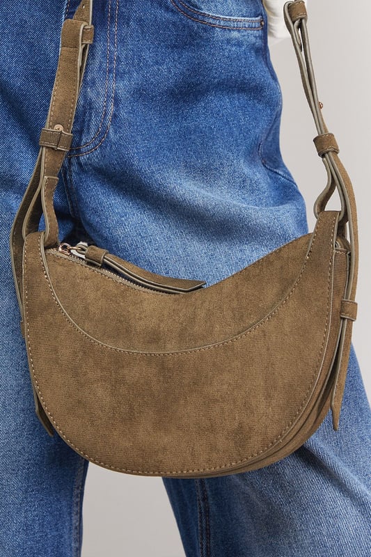 Distinctive half-moon silhouette for a contemporary aesthetic
        Soft faux suede texture adds a luxurious touch to casual outfits
        Adjustable crossbody strap for comfortable all-day wear
        Secure zip-top closure to keep essentials safe
        Compact yet spacious enough for daily necessities
    
    The Relly Faux Suede Half Moon Crossbody Bag combines practicality with feminine charm, embodying Oasis's signature style. The curved silhouette creates a soft, modern look that pairs beautifully with both casual and smart-casual ensembles. Style with relaxed denim and a floaty blouse for daytime outings, or match with a floral day dress for garden parties and family gatherings. The versatile design makes it perfect for weekend shopping trips, coffee dates, or casual lunches. The adjustable strap allows for customised wear, while the interior provides just enough room for your phone, wallet, keys and lipstick. This bag effortlessly transitions from day to evening, making it an essential addition to your accessory collection for those moments when you want to travel light without compromising on style.