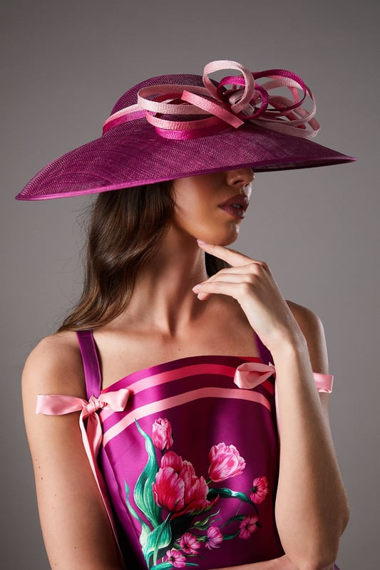 Dramatic wide brim design for maximum impact at special occasions
        Statement bow loop detail adds a touch of artistic flair
        Crafted from natural Abaca fabric with a textured finish
        Versatile one-size design suitable for various hairstyles
        Lightweight construction ensures comfortable wear throughout the day
    
    Make a sophisticated entrance at your next special event with this stunning wide brim hat. The Lisa Tan Bow Loop design showcases exceptional craftsmanship with its sculptural silhouette and artfully arranged bow detail that creates visual interest from every angle. Perfect for weddings, race days and garden parties, this hat pairs beautifully with fitted dresses or tailored ensembles as shown by our model. The natural Abaca construction offers a refined texture that complements formal attire whilst maintaining a contemporary edge. Style with an elegant updo to showcase the hat's dramatic proportions, or wear with loose waves for a more relaxed interpretation. Complete your look with statement earrings and a clutch bag in complementary tones for a cohesive ensemble that reflects true British occasion dressing.