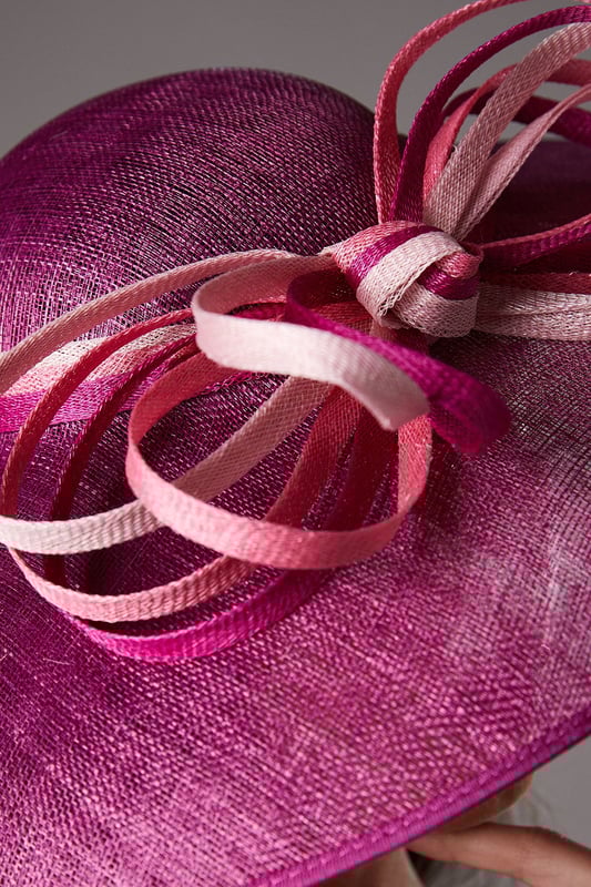 Dramatic wide brim design for maximum impact at special occasions
        Statement bow loop detail adds a touch of artistic flair
        Crafted from natural Abaca fabric with a textured finish
        Versatile one-size design suitable for various hairstyles
        Lightweight construction ensures comfortable wear throughout the day
    
    Make a sophisticated entrance at your next special event with this stunning wide brim hat. The Lisa Tan Bow Loop design showcases exceptional craftsmanship with its sculptural silhouette and artfully arranged bow detail that creates visual interest from every angle. Perfect for weddings, race days and garden parties, this hat pairs beautifully with fitted dresses or tailored ensembles as shown by our model. The natural Abaca construction offers a refined texture that complements formal attire whilst maintaining a contemporary edge. Style with an elegant updo to showcase the hat's dramatic proportions, or wear with loose waves for a more relaxed interpretation. Complete your look with statement earrings and a clutch bag in complementary tones for a cohesive ensemble that reflects true British occasion dressing.